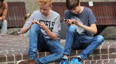 Twee kinderen die op straat zitten met aandacht op hun telefoons.