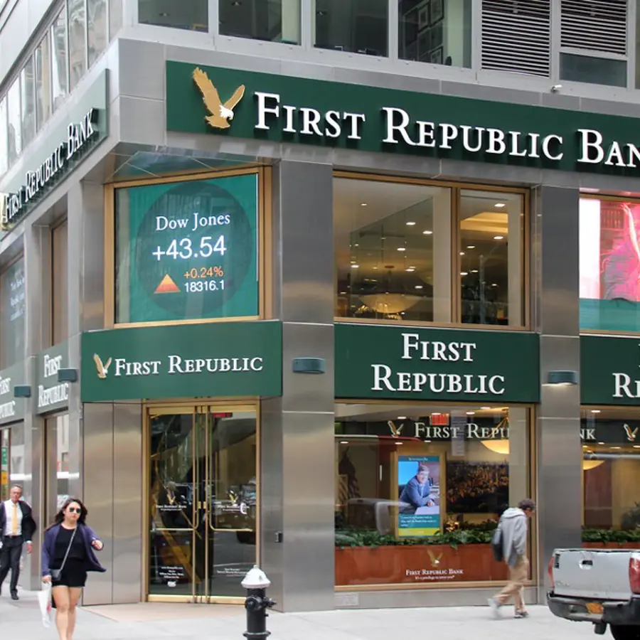 Een foto van de buitenmuur van de "First Republic Bank" in New York City, met groen-gouden letters op een roestvrijstalen gevel en digitale billboards die reclamebeelden weergeven.
