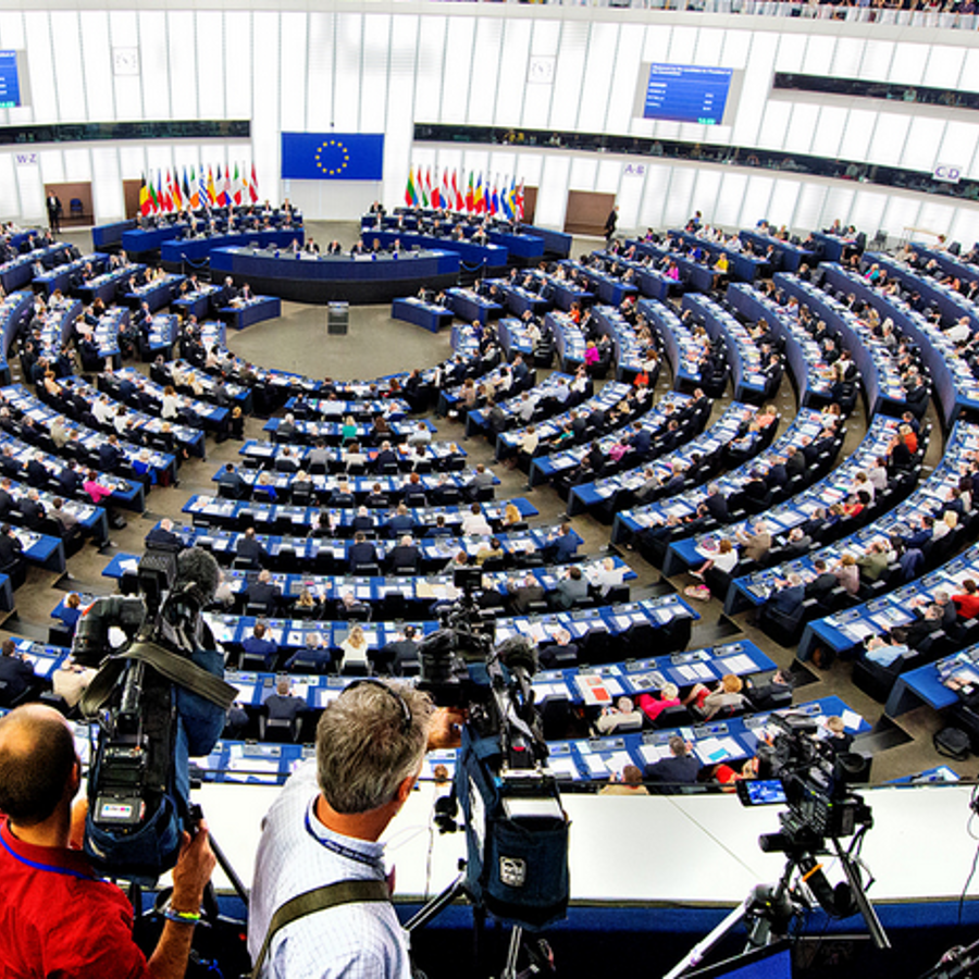 Vergadering in het Europees Parlement met volle zaal en cameramensen op de voorgrond.